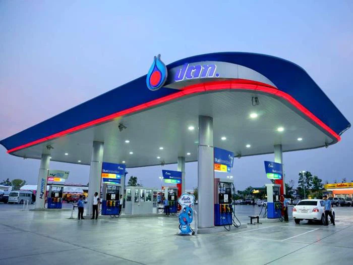 Station-service PTT moderne avec pompes à carburant, éclairage LED et clients en plein ravitaillement au crépuscule.