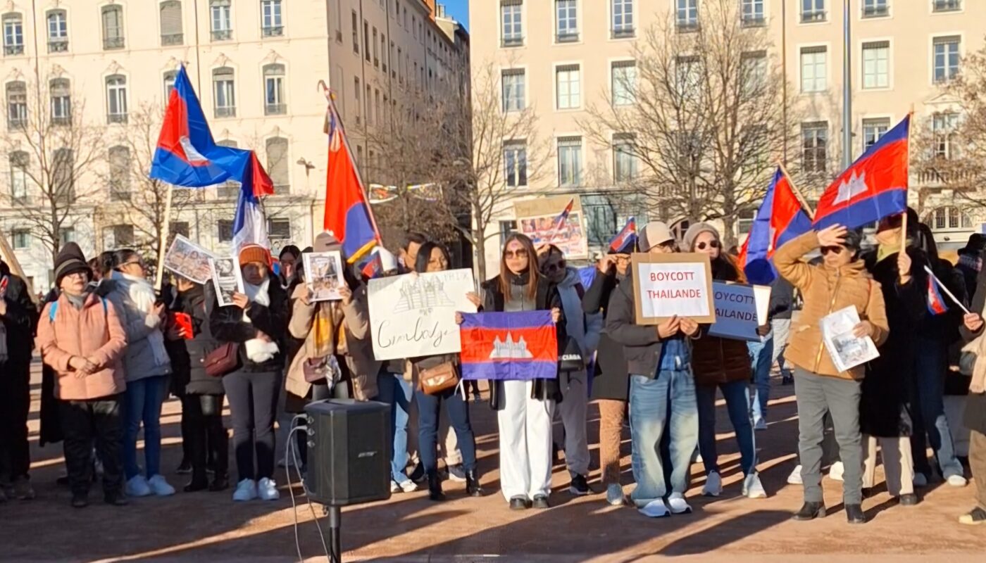 Rassemblement pacifique de la communauté cambodgienne à Lyon, place Bellecour, avec des manifestants tenant des drapeaux du Cambodge et des pancartes demandant justice, reconnaissance des agressions et paix durable pour le Cambodge.