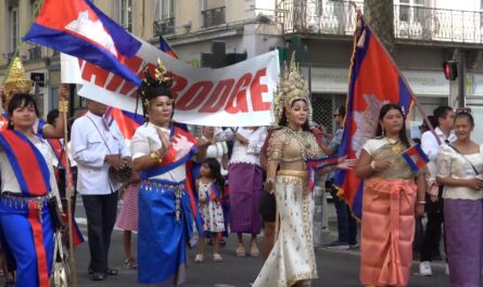 Défilé de la communauté cambodgienne à Lyon lors de la Fête des Bannières du Monde. Des femmes et des enfants portent des costumes traditionnels khmers, des couronnes ornées et des drapeaux du Cambodge, avançant ensemble dans la rue, symbole de fierté culturelle et de transmission.